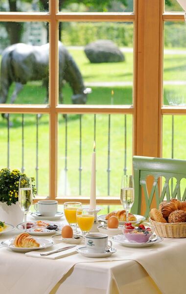 Blick in den Frühstücksraum in die Salzburger Stube des Hotel  Gut Ising am Chiemsee wo ein eingedeckter Frühstückstisch mit Blick in den Innenhof zu sehen ist.