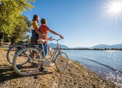 Zwei Personen stehen mit Fahrrädern an den Ufern des Chiemsees bei herrlichen Sonnenschein.